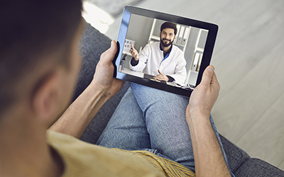 Online medical consultation for patients. Doctor man video call using laptop talks with male patient sitting on the sofa at home.