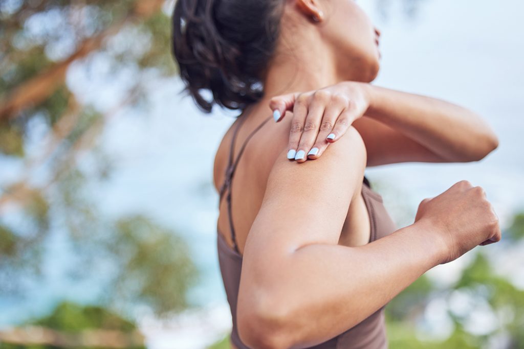 Woman holding shoulder in pain while exercising outdoors, representing joint pain relief and orthopedic care