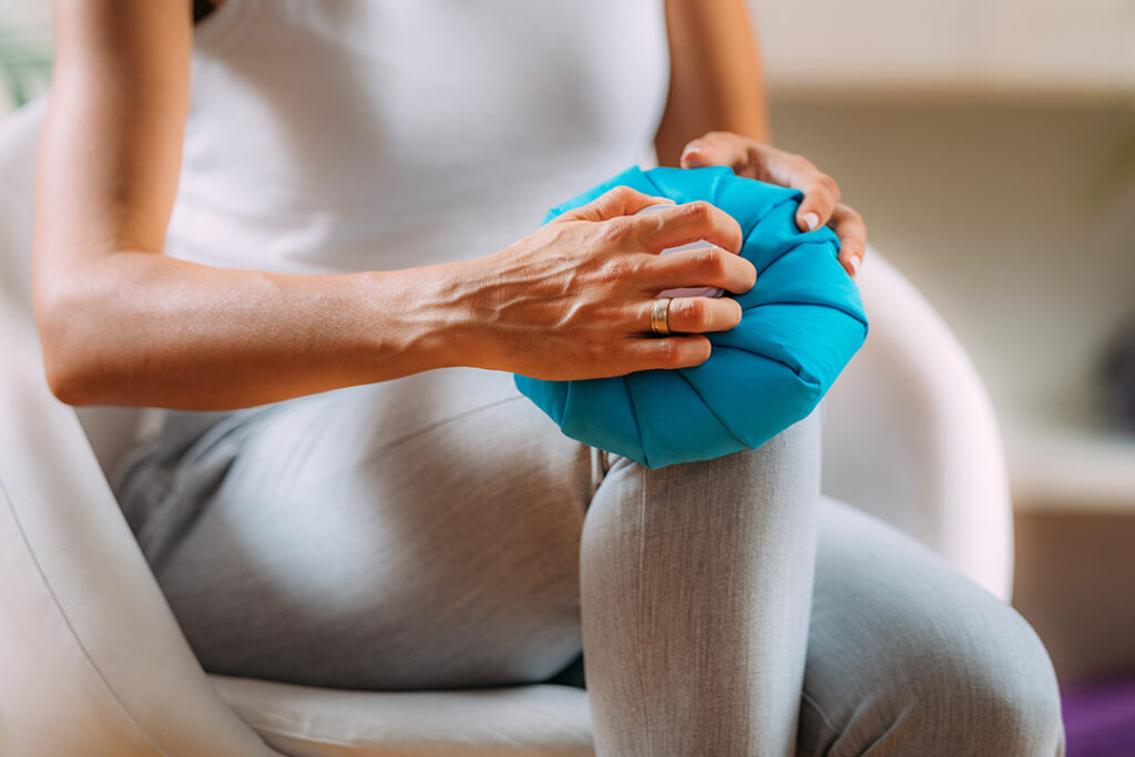 Woman applying ice pack for knee pain relief during home treatment for inflammation and swelling